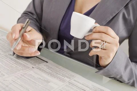 Businesswoman taking notes,holding a cup of coffee, mid section Stock Photos