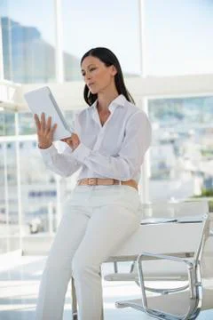 Businesswoman using a digital tablet while sitting on a table in an office Stock Photos