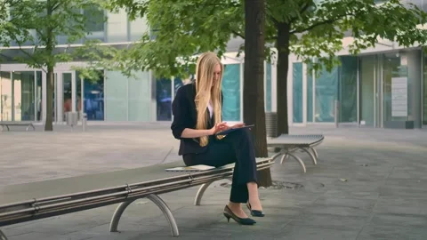 Businesswoman using tablet while seated on bench in urban office patio Stock Footage 340270653