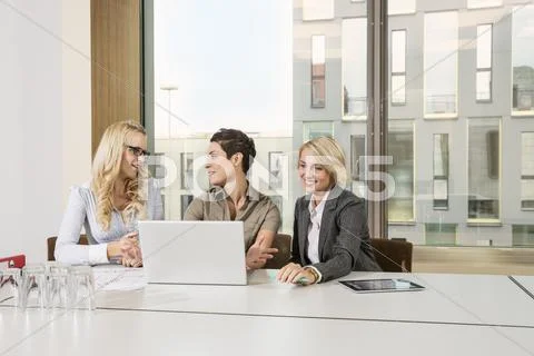 Businesswomen Sitting At Conference Table Using Laptop