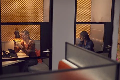Businesswomen Working Late In Individual Office Cubicles Using Laptop And Stock Photos