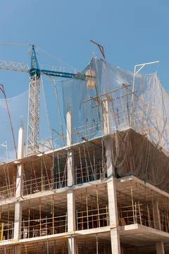 Bustling construction site with a towering crane and protective netting under a Stock Photos