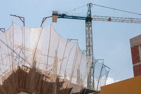 Bustling construction site with a towering crane and protective netting under a Stock Photos