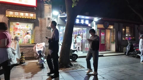 A bustling street corner in Beijing at nighttime with warm lights illuminating Stock Footage 337307136