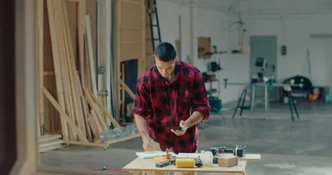 Busy carpenter working in the workshop while holding a mobile phone and write Stock Footage 199619134