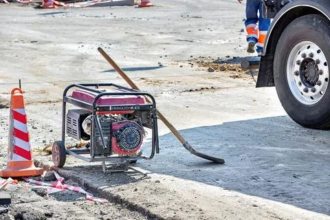 A busy construction site features a generator near safety cones, with workers Stock Photos