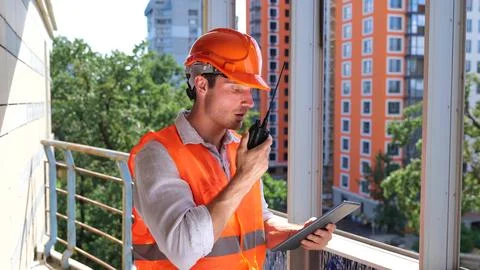 Busy construction worker talking on walkie-talkie while looking at digital Stock Photos