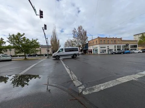 Busy downtown intersection with passing traffic, vintage storefronts Stock Photos