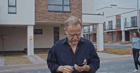 Busy elder man using smartphone outdoor asking for help of pretty young girls Stock Footage 114935869