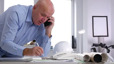 Busy Engineer in Office Talk to Mobile and Write in Agenda Technical Data Stock Footage 98588125