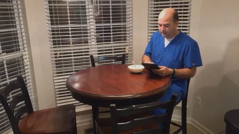 Busy male nurse using tablet computer at breakfast table before heading off to 動画素材 81554929