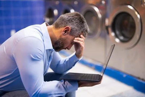 Busy man doing laundry and working on laptop. Stressed employee multitasking Stock Photos