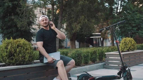 Busy man with e-scooter parked nearby talking on phone while working on laptop Stock-Footage 229258152