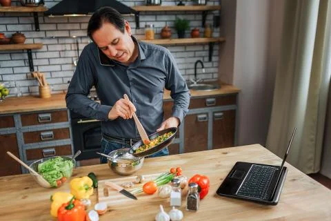 Busy man stand at table in kitchen and blend eggs. He talk on phone and look Stock-Fotos