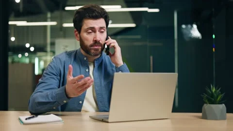 Busy man talking on smartphone while sitting in office at desk with computer Stock-Footage 266972853