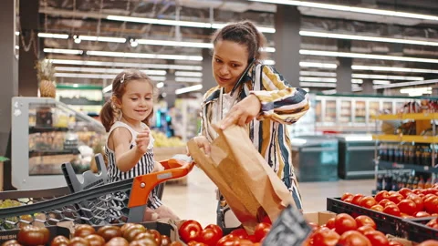 Busy mom in the supermarket talking on the phone and putting tomatoes in a paper Stock Footage