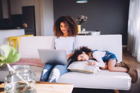 Busy mom working with laptop and her daughter on couch Stock Photos