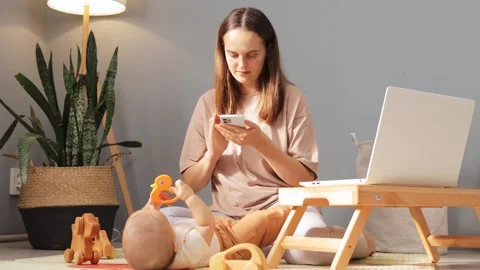 Busy mother using mobile phone while babysitting her daughter or son and working Video stock 287172902