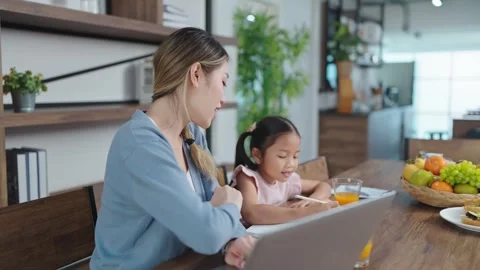 Busy mother working on laptop while caring teaching homework to daughter at home Stock Footage 243751628