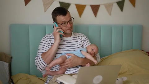 Busy multitasking father working remotely from home on laptop while holding his Video stock 344282195