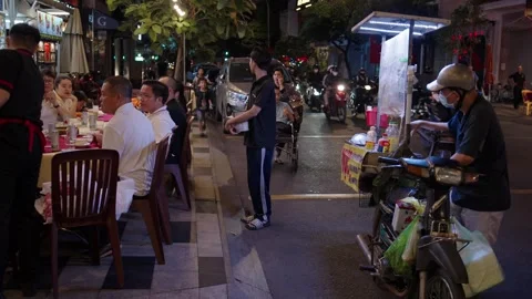Busy Night Sidewalk Restaurant With Diners and Street Vendor Along Road in Asia Stock Footage 331786206