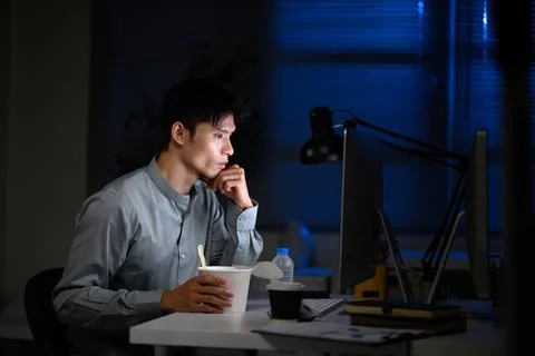 Busy office worker has quick dinner at desk during overtime Stock Photos