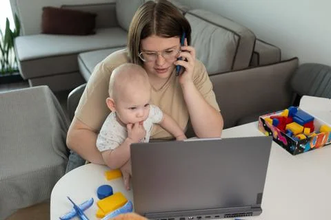 A busy parent struggles to balance work and caring for their baby while working Stock Photos