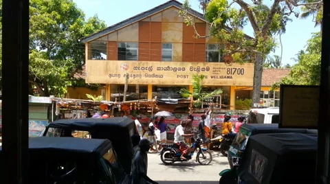 Busy street with cars, tuk tuks, pedestrians passing by post office and market Stock Footage