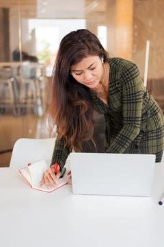 Busy woman taking notes while using laptop Stock Photos