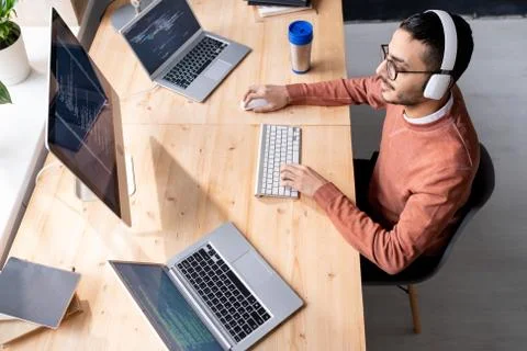 Busy young software developer in headphones sitting by table and typing Stock Photos
