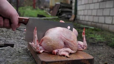 A butcher cuts up a chicken carcass with a kitchen cleaver on a cutting board Stock Footage 326015387