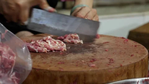 Butcher cuts meat into thin slices with a knife on a wooden chopping block while Stock Footage 332029656