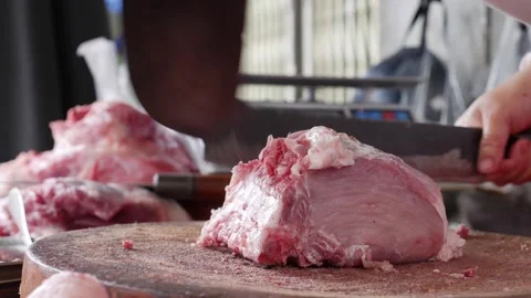 Butcher forcefully chops meat with bone using a cleaver on a round wooden Vidéo 332859566