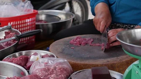 Butcher slices raw meat into thin pieces using a heavy knife on a round wooden Stock Footage 330724834