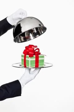 A butler taking the lid off a domed tray, revealing a gift, focus on hands Stock Photos