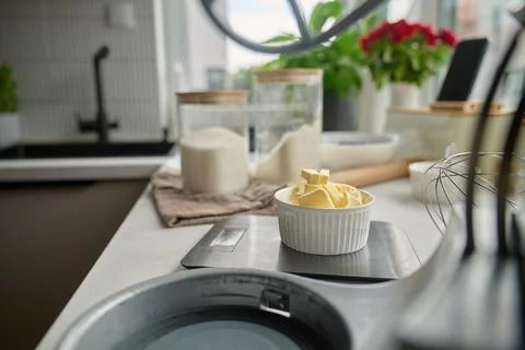 Butter cubes in a bowl on a kitchen scale with flour and baking tools Stock Photos