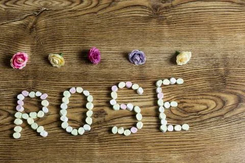 Button roses and the text rose formed with marshmallows on wooden background. Stock Photos