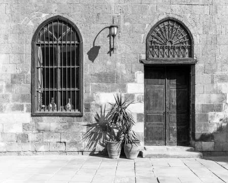 BW shot of abandoned stone bricks wall with wooden door, wrought iron window Stock Photos