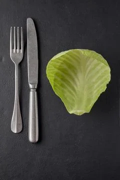 Cabbage leaf and cutlery fork with knife on black table. weight loss diet c.. Stock Photos