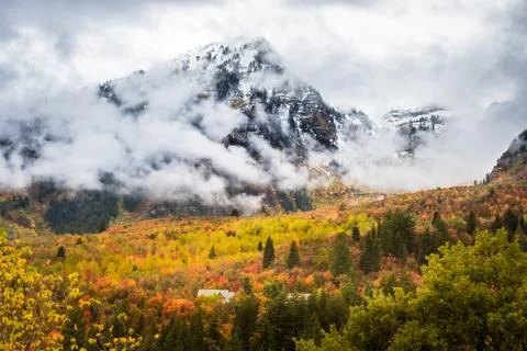 A Cabin in a Forest with Fall Colored Leaves Below Cloud Covered Mountains Wi Foto stock