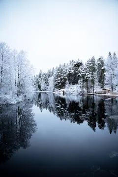 Cabin by river surrounded by snow covered forest Stock Photos