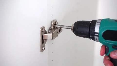 Cabinet hinge installation. Screwing screw with screwdriver on wooden furniture. Stock Footage 256067397