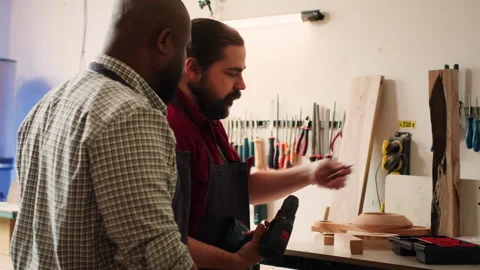 Cabinetmaker teaching apprentice to drill hole into timber block Video stock 271213522