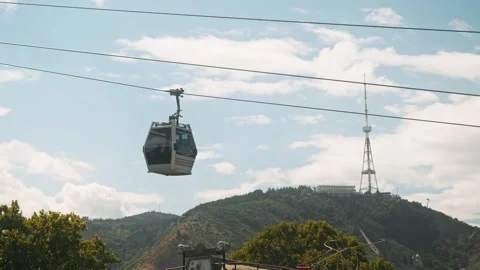 Cable car ascends rope, against backdrop of Tbilisi city and television tower Stock Footage 292255866