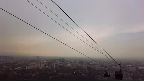Cable car cabins move along the lift against the backdrop of the city at sunset Video stock 236813604