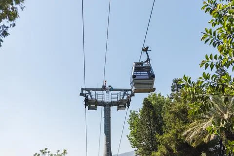 A cable car glides along its overhead track, surrounded by green trees and .. Stock Photos