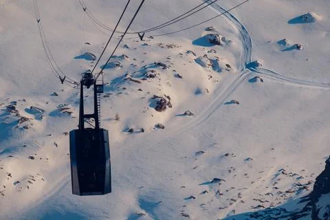 Cable car going down to the valley between the snow-capped mountains Stock Photos