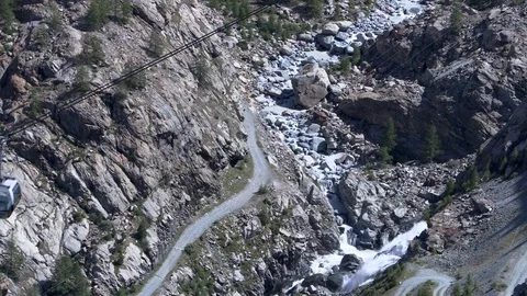 A cable car passes over a river trickling down from the Swiss Alps Stock Footage 114838787