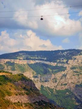Cable car suspended between mountain peaks under partly cloudy skies Stock Photos