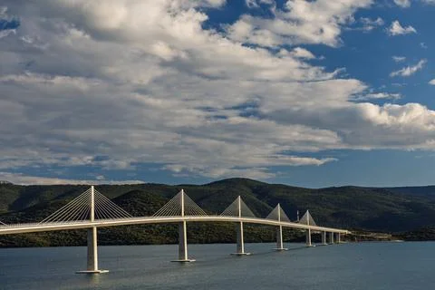 Cable-Stayed Bridge Spanning Calm Water With Mountain Landscape and Golden .. Stock Photos